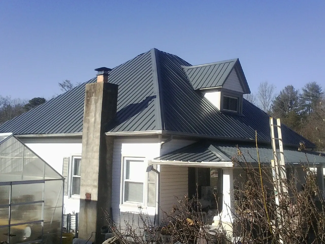 Dark blue standing seam metal roof on a white farmhouse with dormer — Slate & Tile Roof Repair by Roofing Brothers in Perrysville
