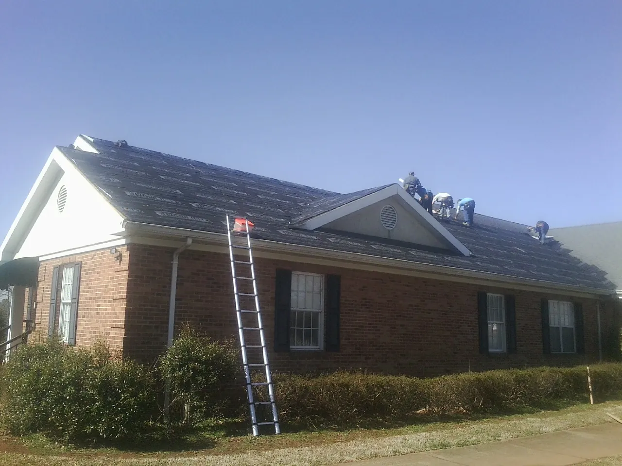 Crew tearing shingles off a brick ranch roof with a ladder set — Metal Roof Repair work by our crew in Perrysville