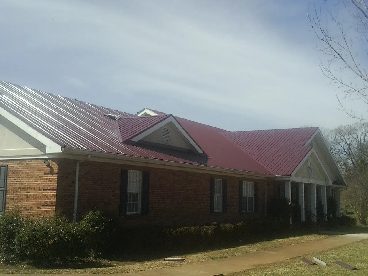 Red metal roof with gabled entries on a long brick building, from a Hail Damage Roof Repair job in Perrysville