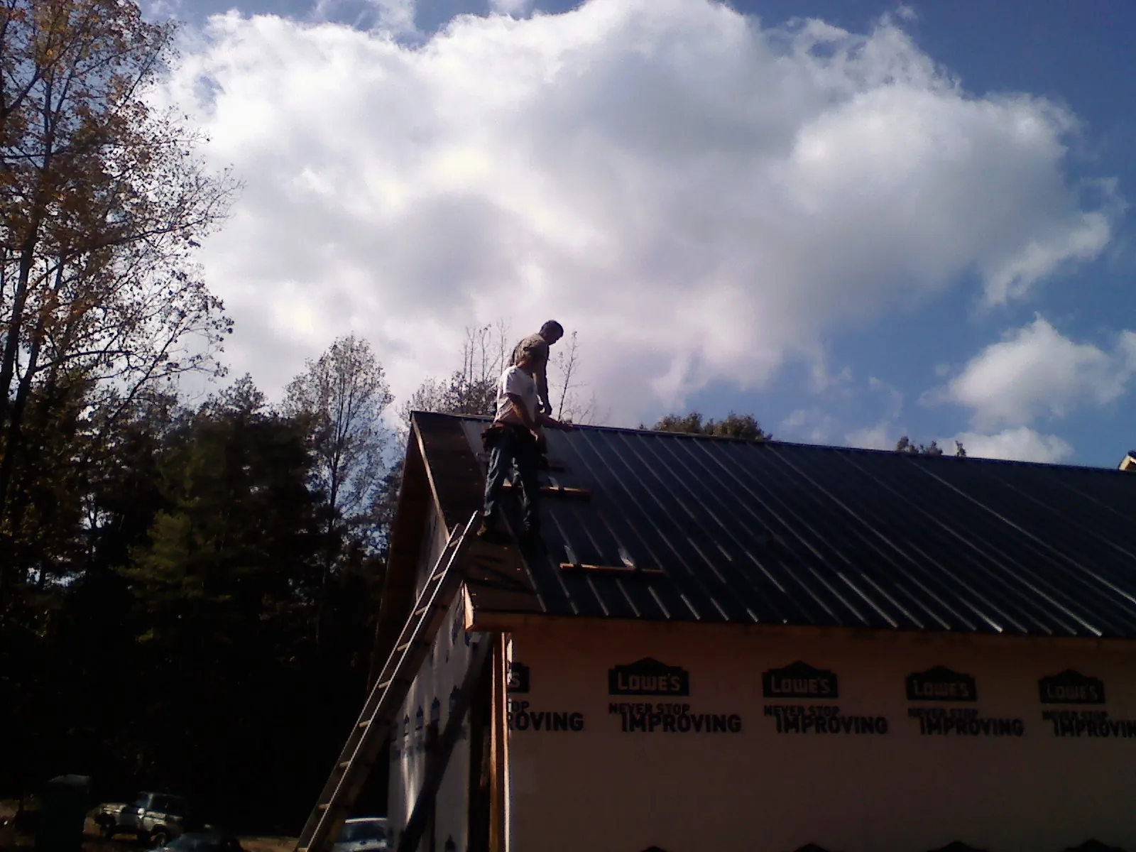 Roofer fastening dark metal panels high against a cloudy sky, from a Roof Inspection job in Perrysville