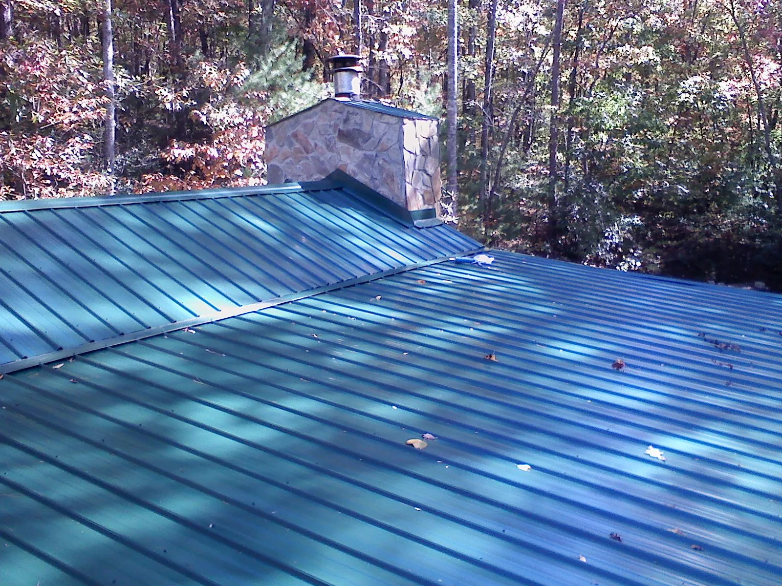 New green metal roof and stone chimney surrounded by autumn woods in Perrysville