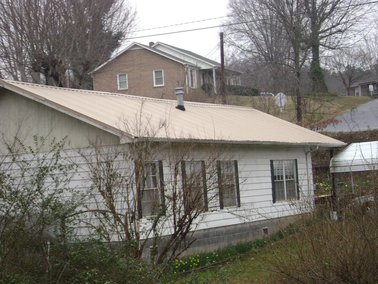 Tan metal roof on a white sided house set into a hillside — Commercial Roofing by Roofing Brothers in Perrysville
